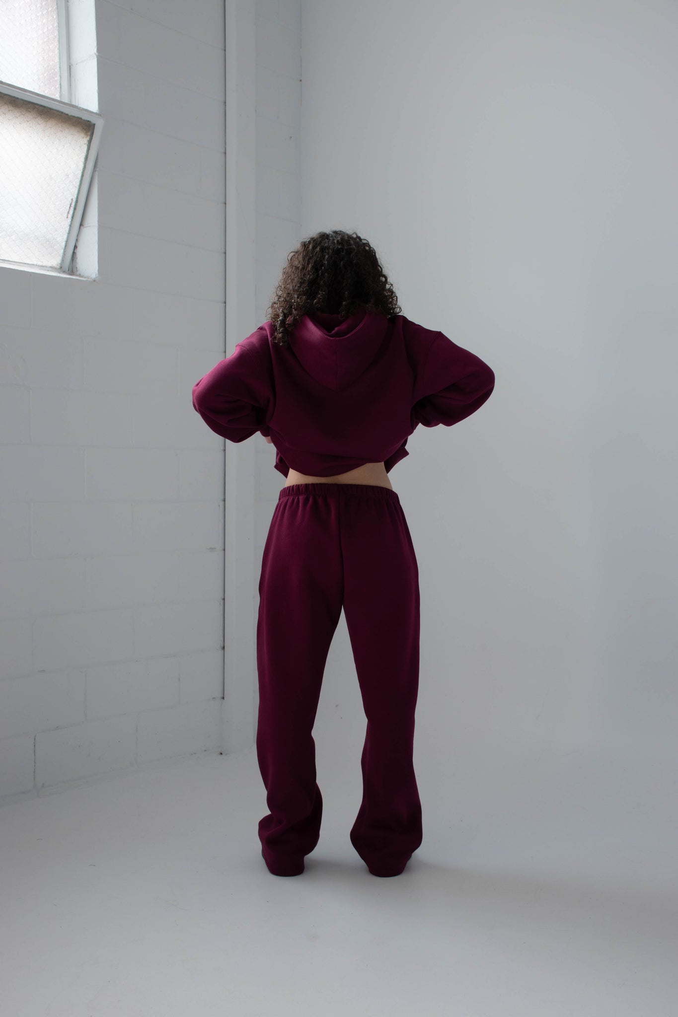 Person wearing a burgundy tracksuit standing in a minimal white room.