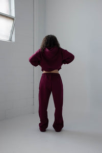 Person wearing a burgundy tracksuit standing in a minimal white room.