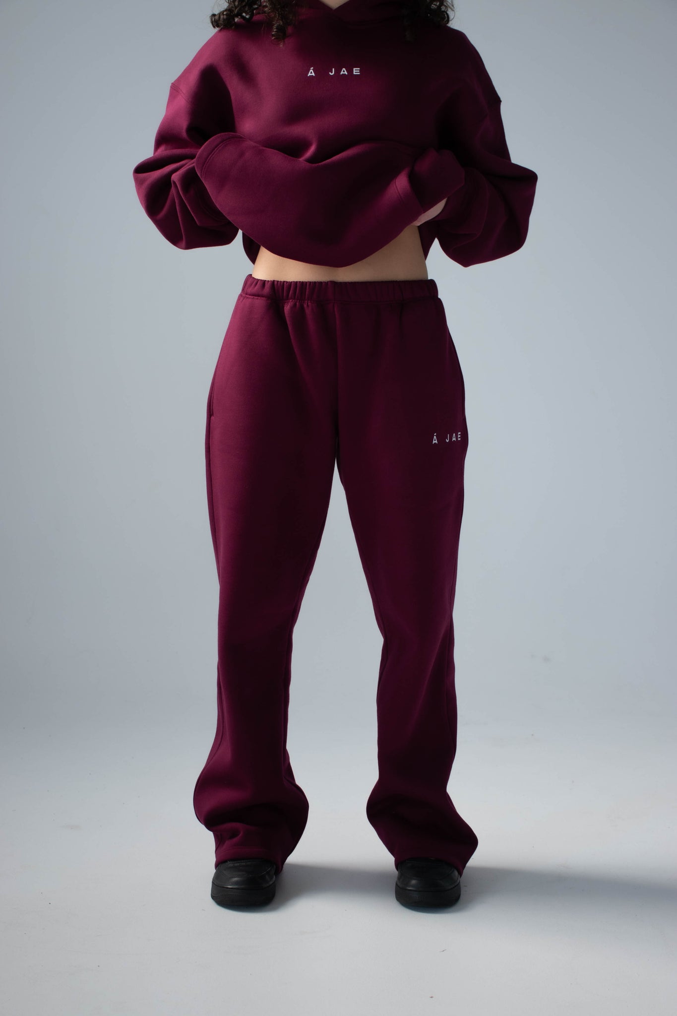 Person wearing a burgundy tracksuit with brand logos on a plain background
