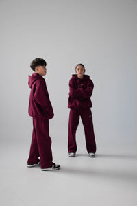 Two people wearing matching maroon tracksuits on a white background
